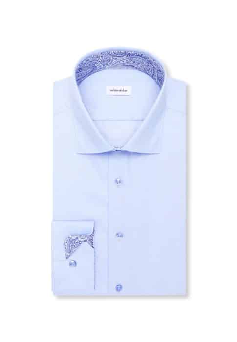 A light blue dress shirt neatly folded, featuring paisley-patterned fabric inside the collar and cuffs, and a white label with text on the inside of the collar.