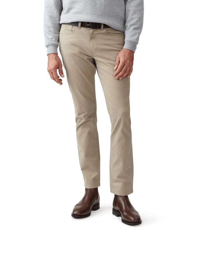 A person wearing light beige trousers, a grey jumper, and dark brown leather boots stands against a plain white background. The photo is cropped from the shoulders down.