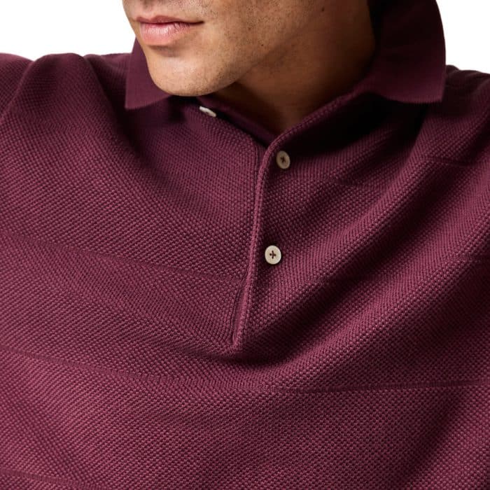 A close-up of a person wearing a textured, dark maroon knitted polo shirt with a collar and off-white buttons. The person's face is partially visible, focusing on the lower half and neck.