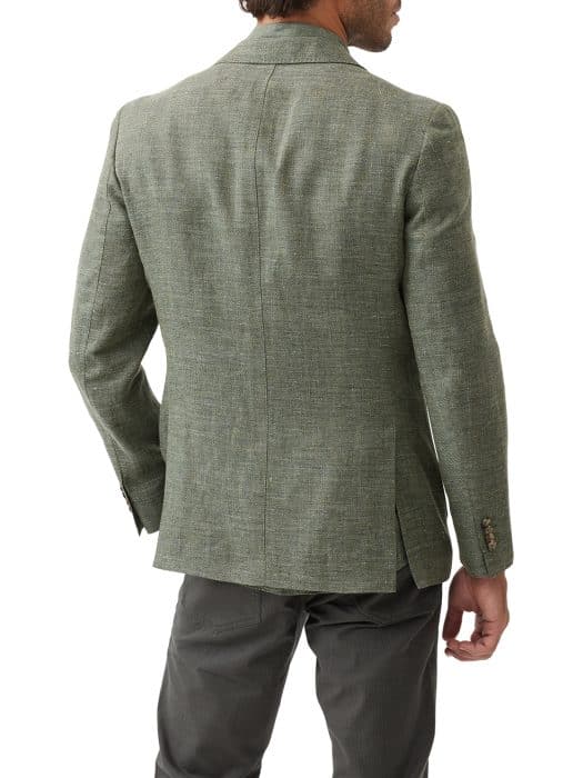 A man is shown from the back wearing a green textured blazer with side vents and dark grey trousers. His right hand is slightly turned outward, and his head is turned slightly to the right.
