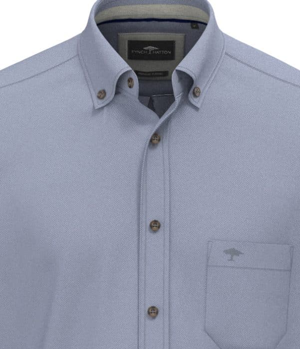 Light blue button-up shirt with a subtle herringbone pattern, brown buttons, and a single chest pocket featuring a small embroidered logo. The shirt has a button-down collar and a visible brand label inside.