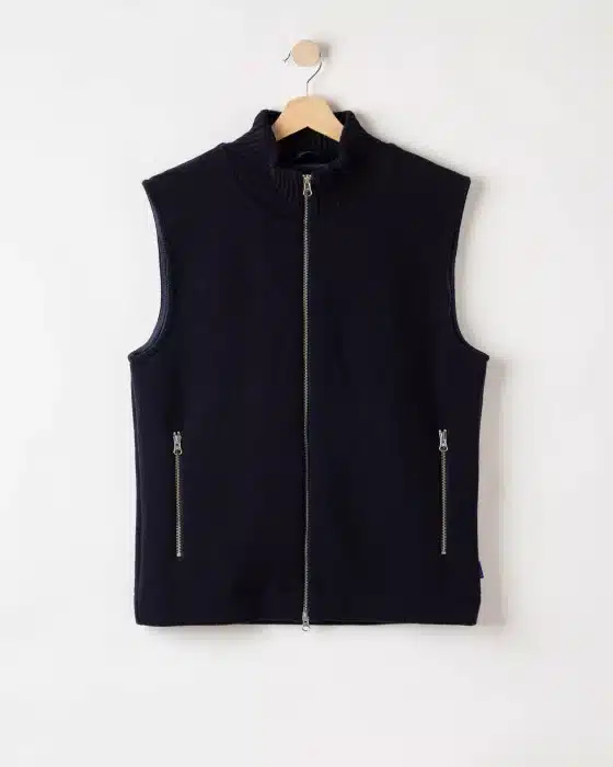 A sleeveless navy blue zip-up gilet with a ribbed collar and two front zipped pockets, hanging on a wooden hanger against a plain white background.