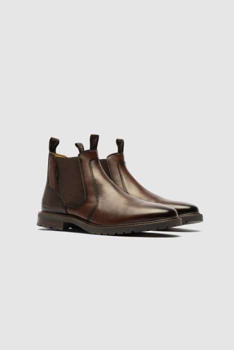 Pair of brown leather Chelsea boots with elastic side panels and pull tabs, displayed on a light grey background. The boots have a sleek, polished finish and slightly pointed toes.
