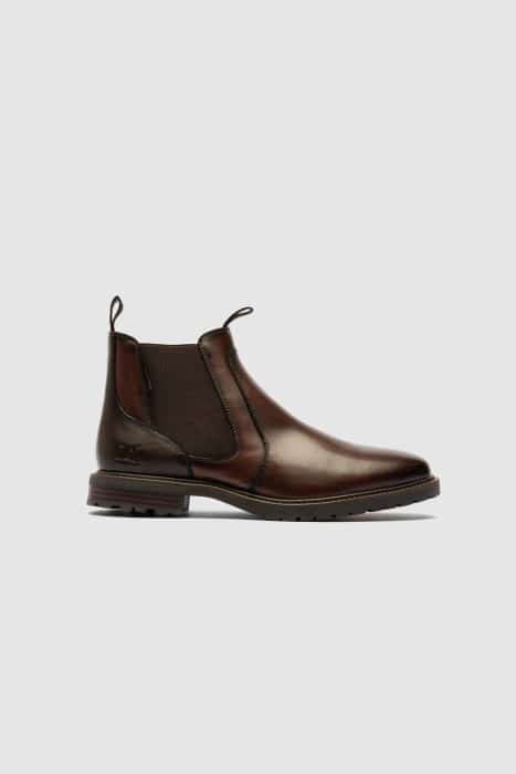 A single brown leather Chelsea boot with elastic side panels, a pull tab at the heel, and a low black sole, displayed on a plain light grey background.