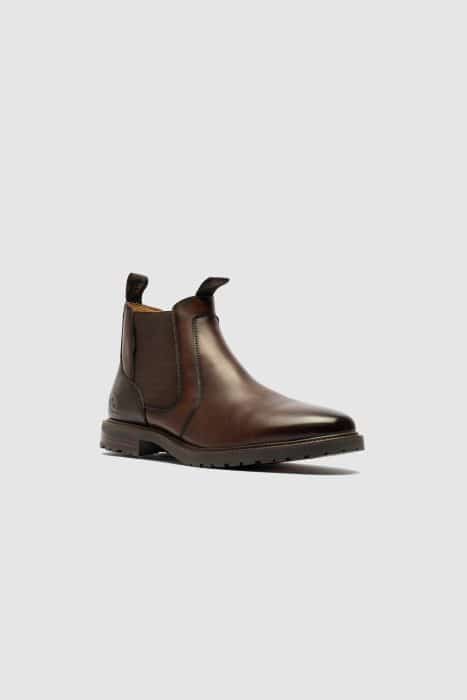 A single brown leather Chelsea boot with elastic side panels, a pull tab at the back, and a low black sole, displayed on a plain light grey background.