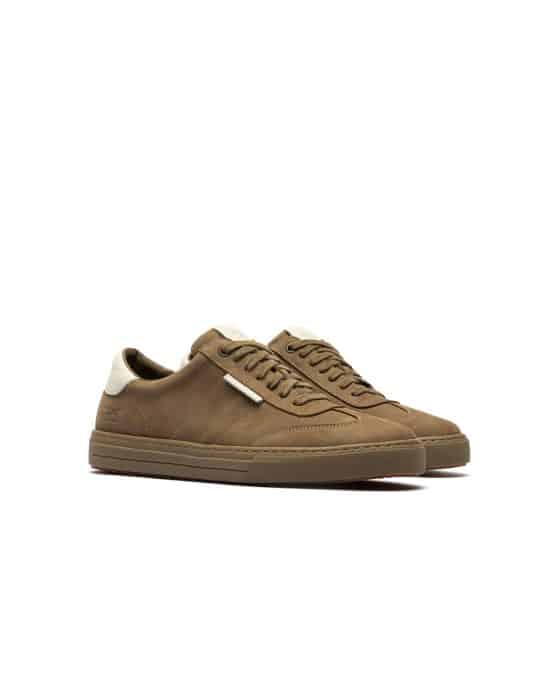 Brown low-top trainers with white accents on the heel and tongue, displayed on a white background. The shoes feature brown laces and a textured brown sole, positioned side by side at a slight angle.