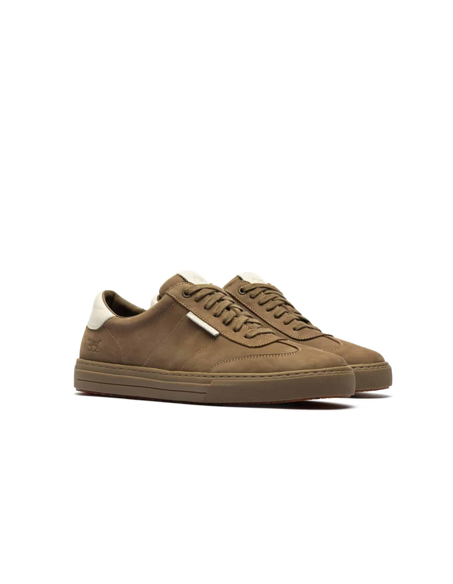 Brown low-top trainers with white accents on the heel and tongue, displayed on a white background. The shoes feature brown laces and a textured brown sole, positioned side by side at a slight angle.