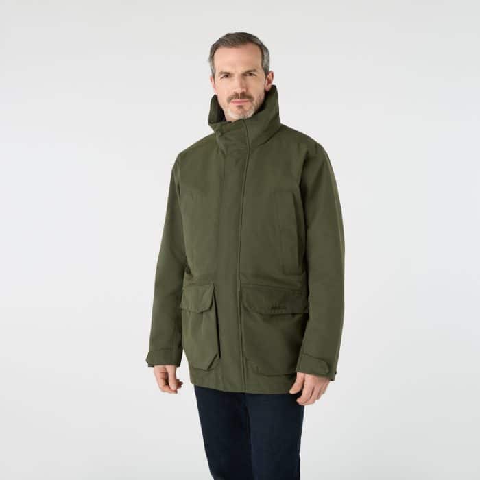 A man wearing an olive green Musto brand jacket with a high collar and front pockets.