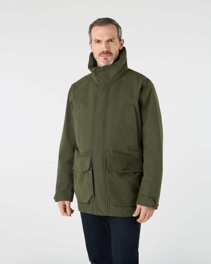 A man wearing an olive green Musto brand jacket with a high collar and front pockets.