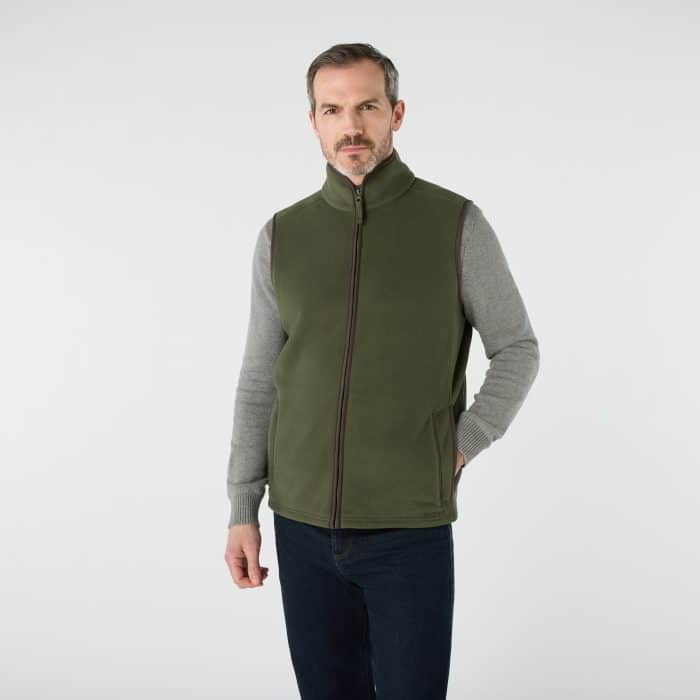A man wearing a grey jumper and an olive green zip-up fleece gilet.