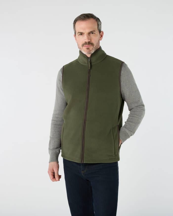 A man wearing a grey jumper and an olive green zip-up fleece gilet.