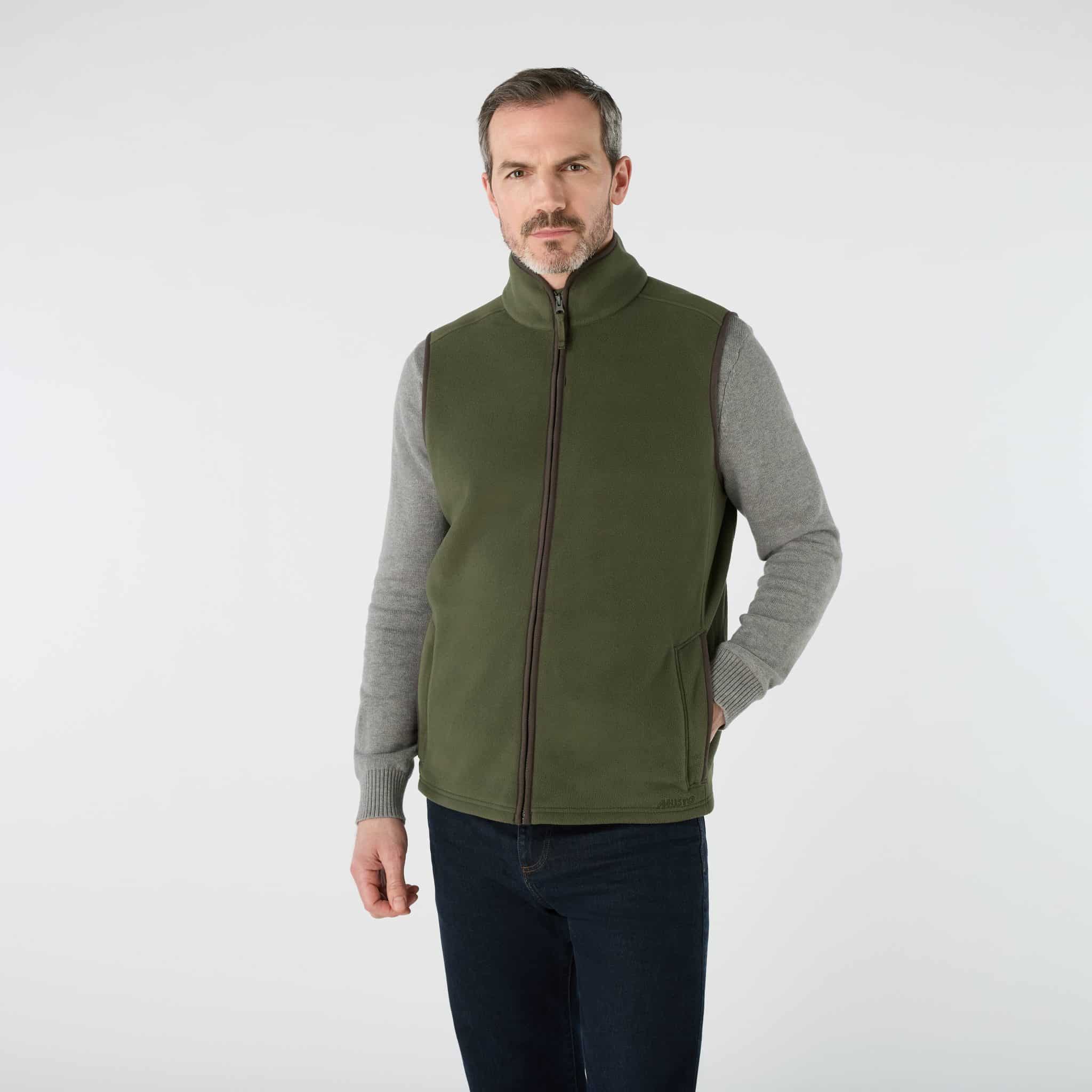 A man wearing a grey jumper and an olive green zip-up fleece gilet.