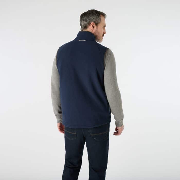 A man viewed from behind, wearing a navy fleece gilet over a grey jumper and dark jeans.
