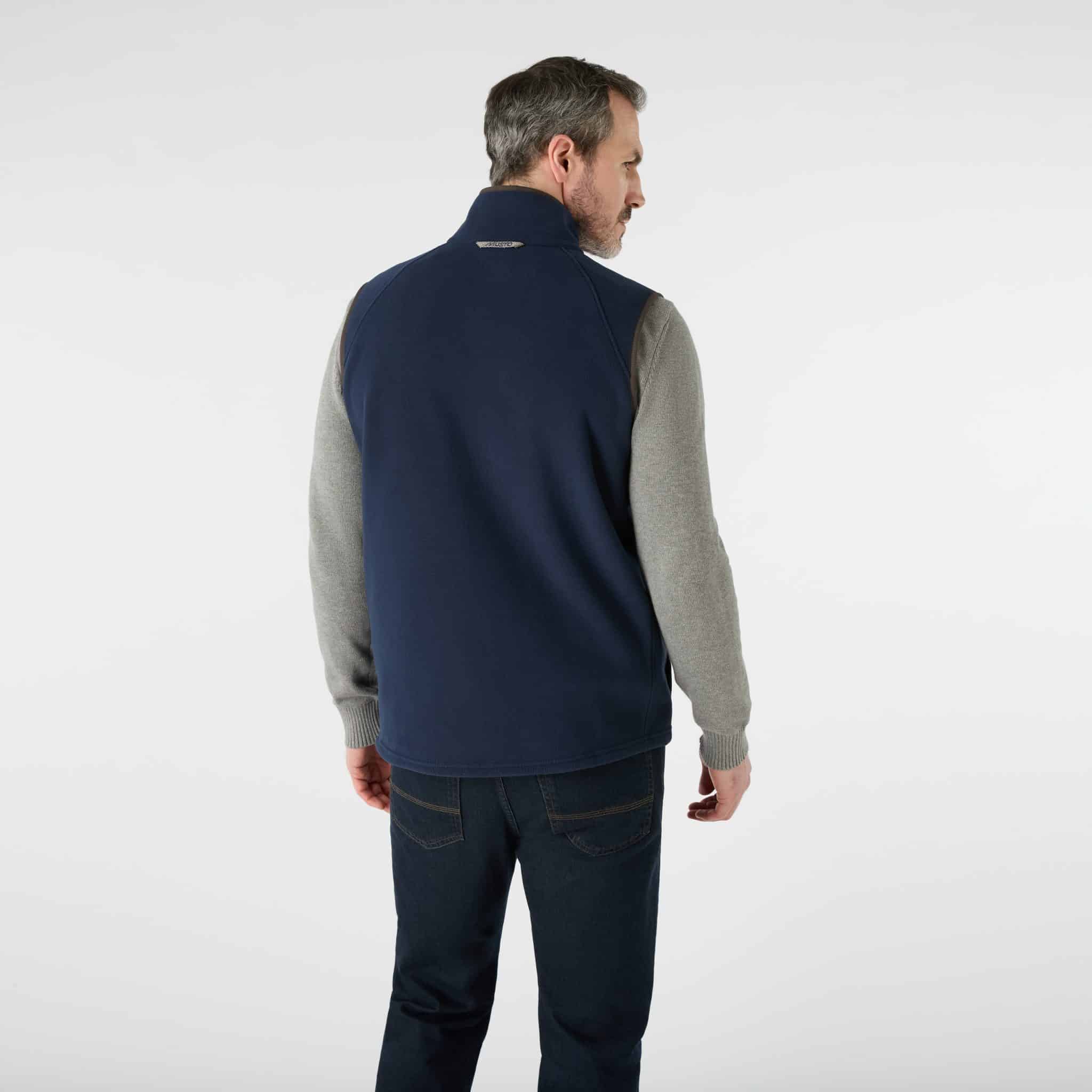 A man viewed from behind, wearing a navy fleece gilet over a grey jumper and dark jeans.