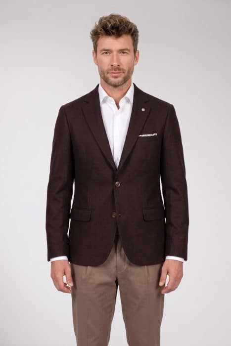 A man wearing a dark brown blazer over a white dress shirt and tan trousers.