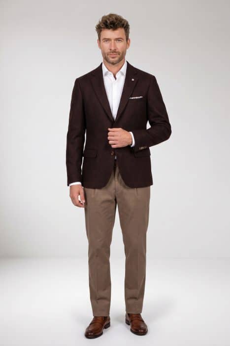 A man wearing a brown blazer, white dress shirt, and tan trousers stands against a white background.