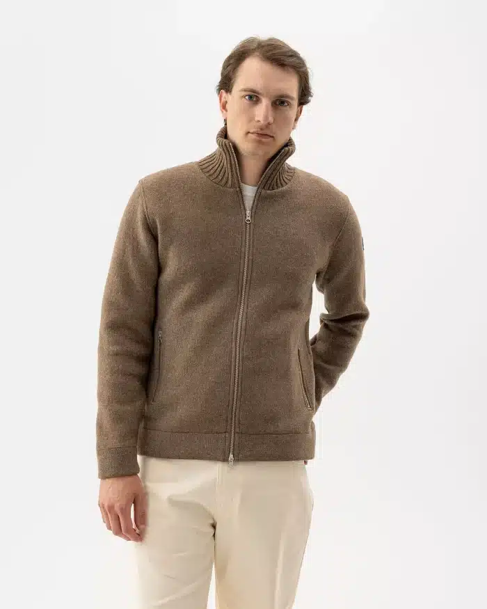 Man wearing a taupe Holebrook zip-up wool jacket with ribbed funnel collar, over a white top and cream trousers