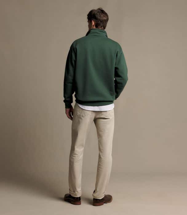 A man seen from behind wearing a green quarter-zip jumper, white vest, and light-coloured jeans.