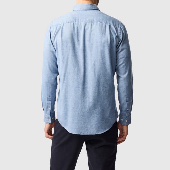 Back view of a person wearing a light blue long-sleeve button-up shirt and dark trousers.