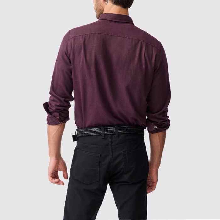 A man from the back wearing a long-sleeved dark purple buttoned-down shirt tucked into black trousers with a dark belt.