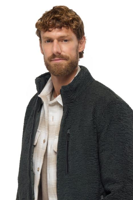 Man wearing a dark grey zip-up fleece jacket over a tan checked shirt.
