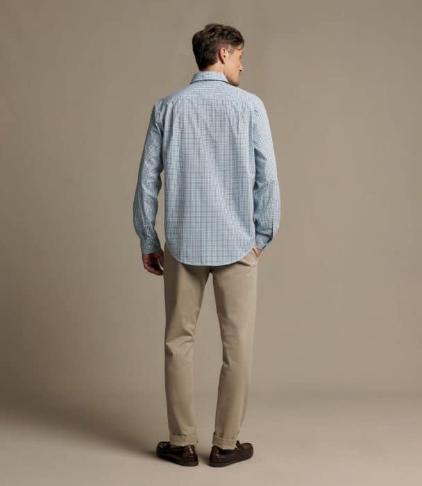A man seen from the back wearing a light blue gingham button-down shirt, tan trousers, and brown leather loafers.