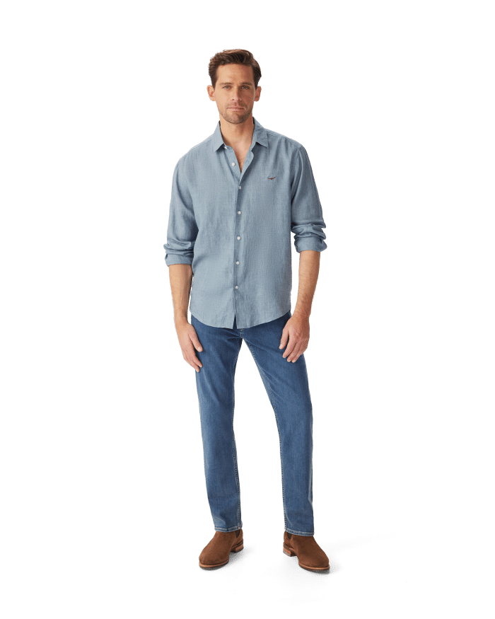 A man wearing a blue button-down shirt, blue jeans, and brown boots.